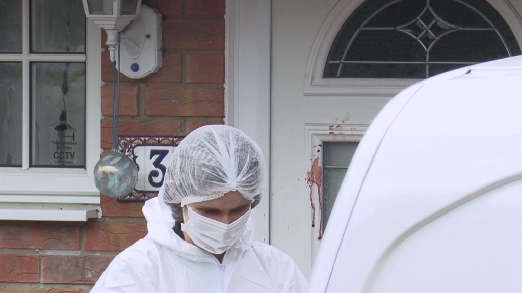 Grim task: A forensics officer in front of the house (below) where blood is seen on the front door